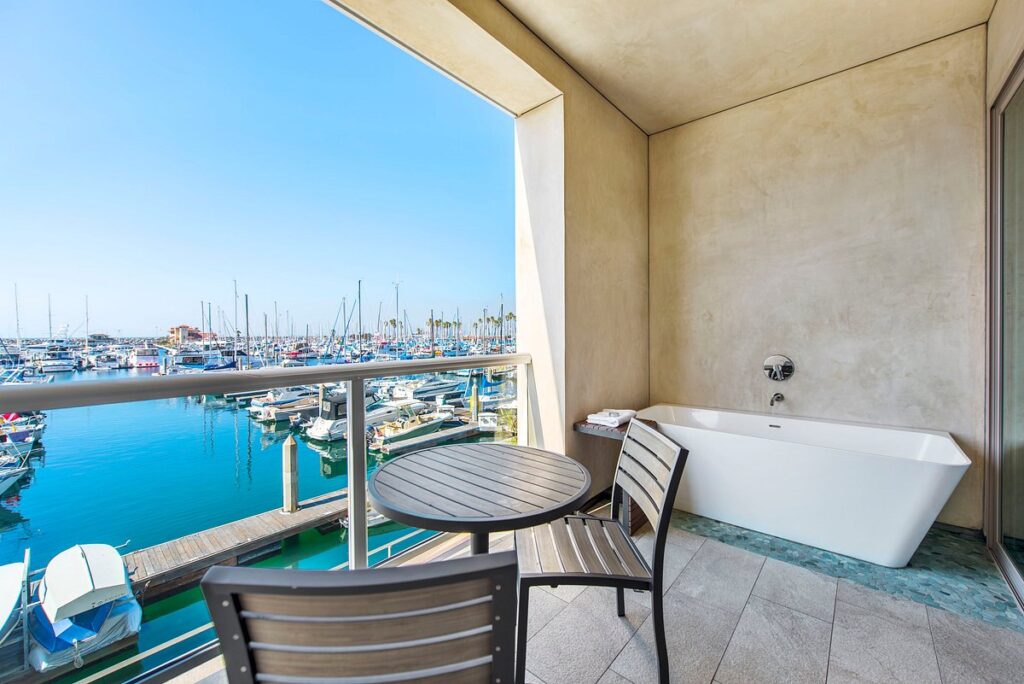 Private balcony with a freestanding bathtub overlooking a marina, outdoor seating, and waterfront views
